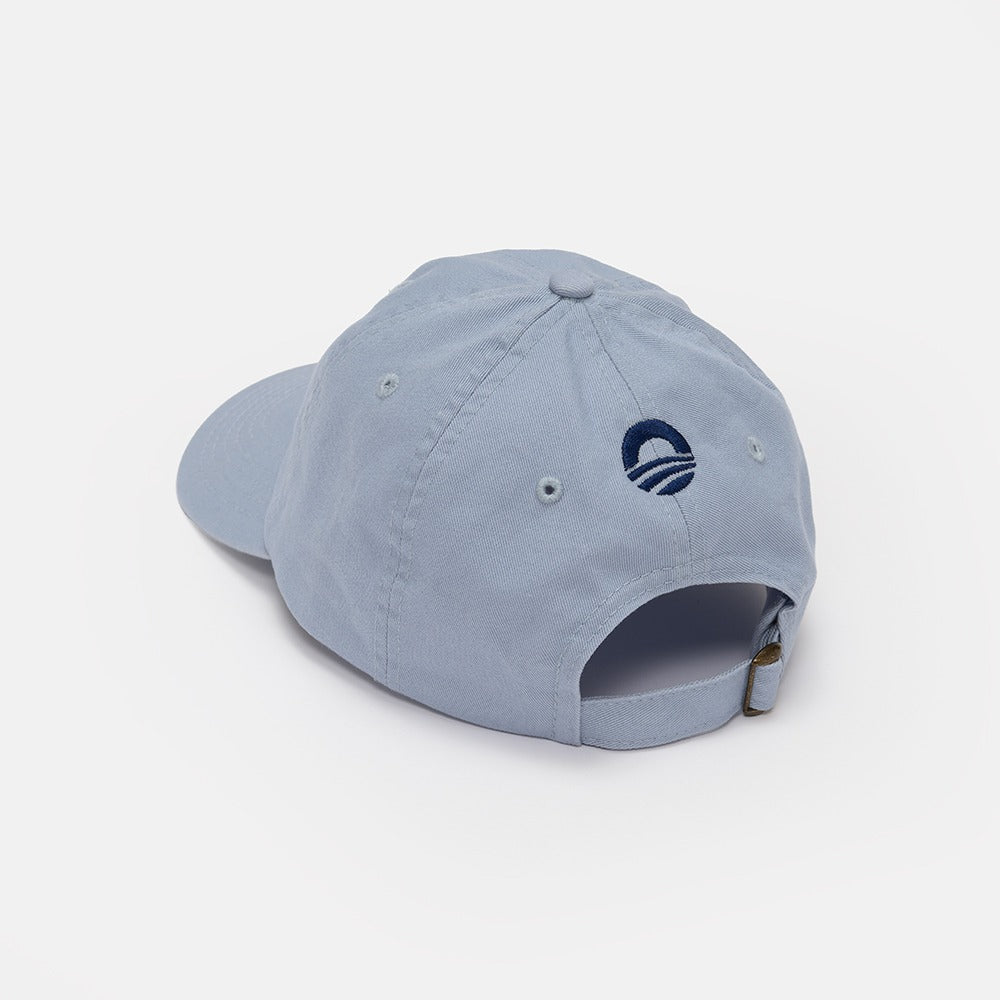 The Obama Presidential Center Hope Cap - Blue is displayed from the back, showing its adjustable metal buckle strap and a small navy embroidered logo above the opening.