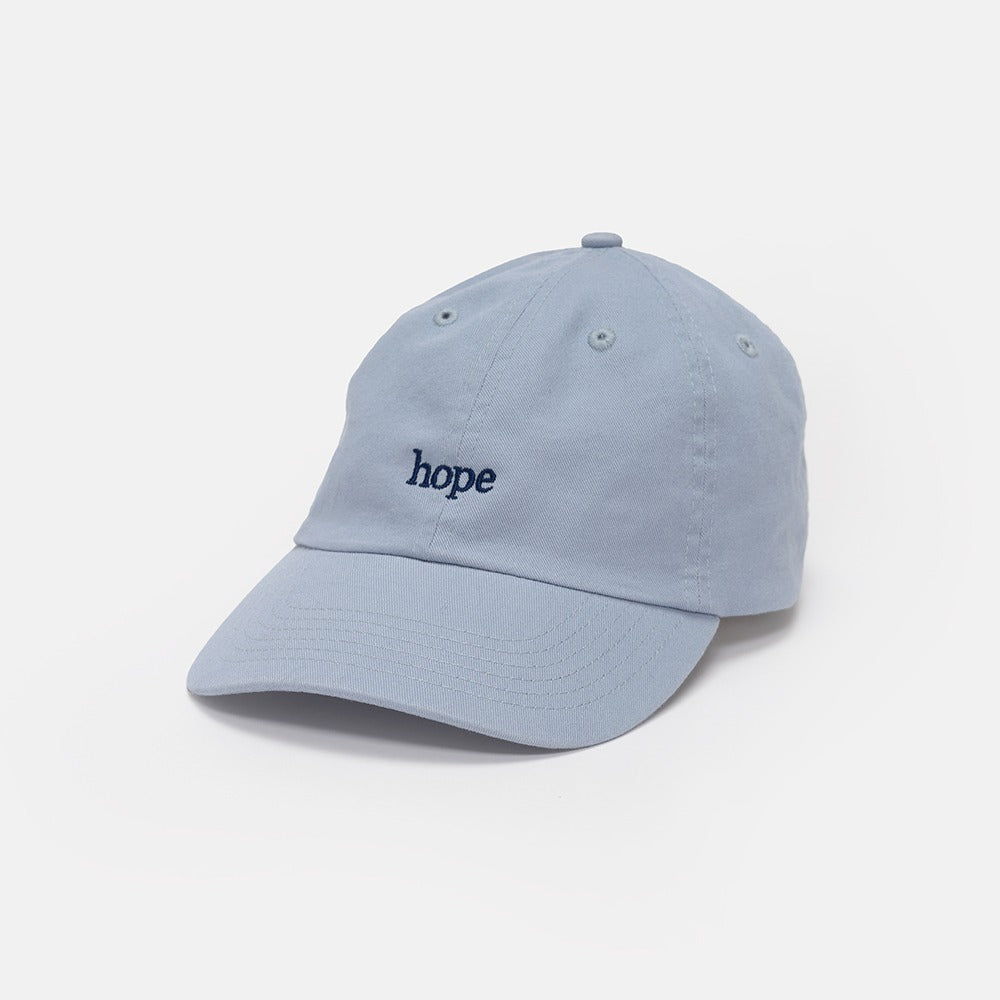 The Obama Presidential Center Hope Cap - Blue features "hope" embroidered in small, black lowercase letters on the front. The light blue cap is shown against a plain white background.
