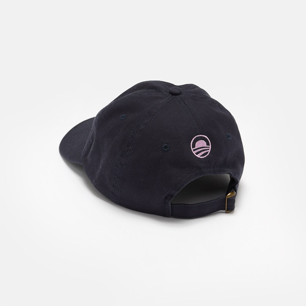 The Obama Presidential Center Imagination Cap in black is shown from the back, highlighting a small pink embroidered logo and an adjustable strap with a brass buckle.