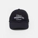 The Obama Presidential Center Embroidered Cap is a black cap with white embroidered text on the front, shown against a plain white background. This official accessory is part of the Obama Foundation collection.