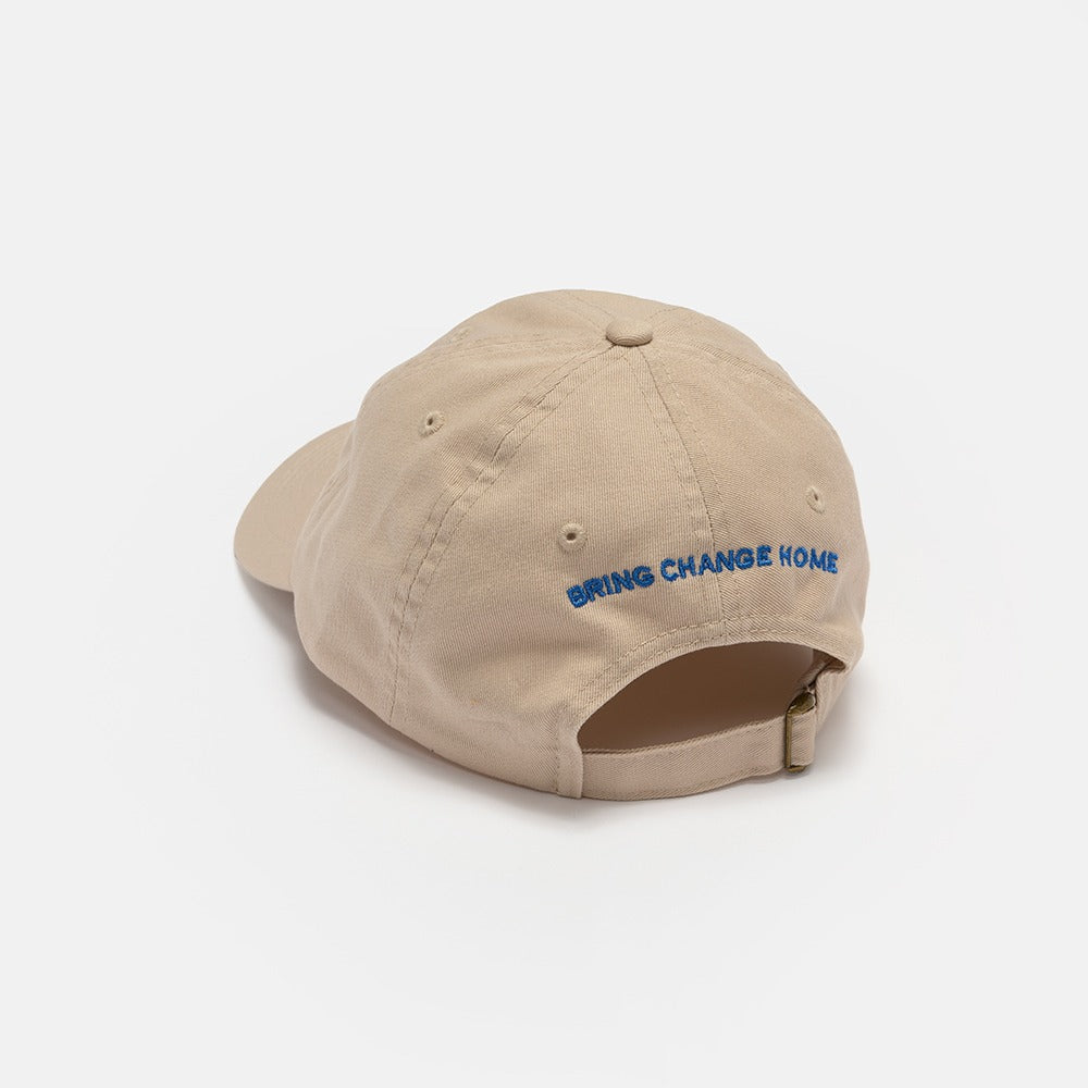 The Obama Presidential Center Symbol Cap is an off-white unisex cotton hat with an adjustable back strap and "BRING CHANGE HOME" embroidered in blue—a stylish accessory for everyday wear.