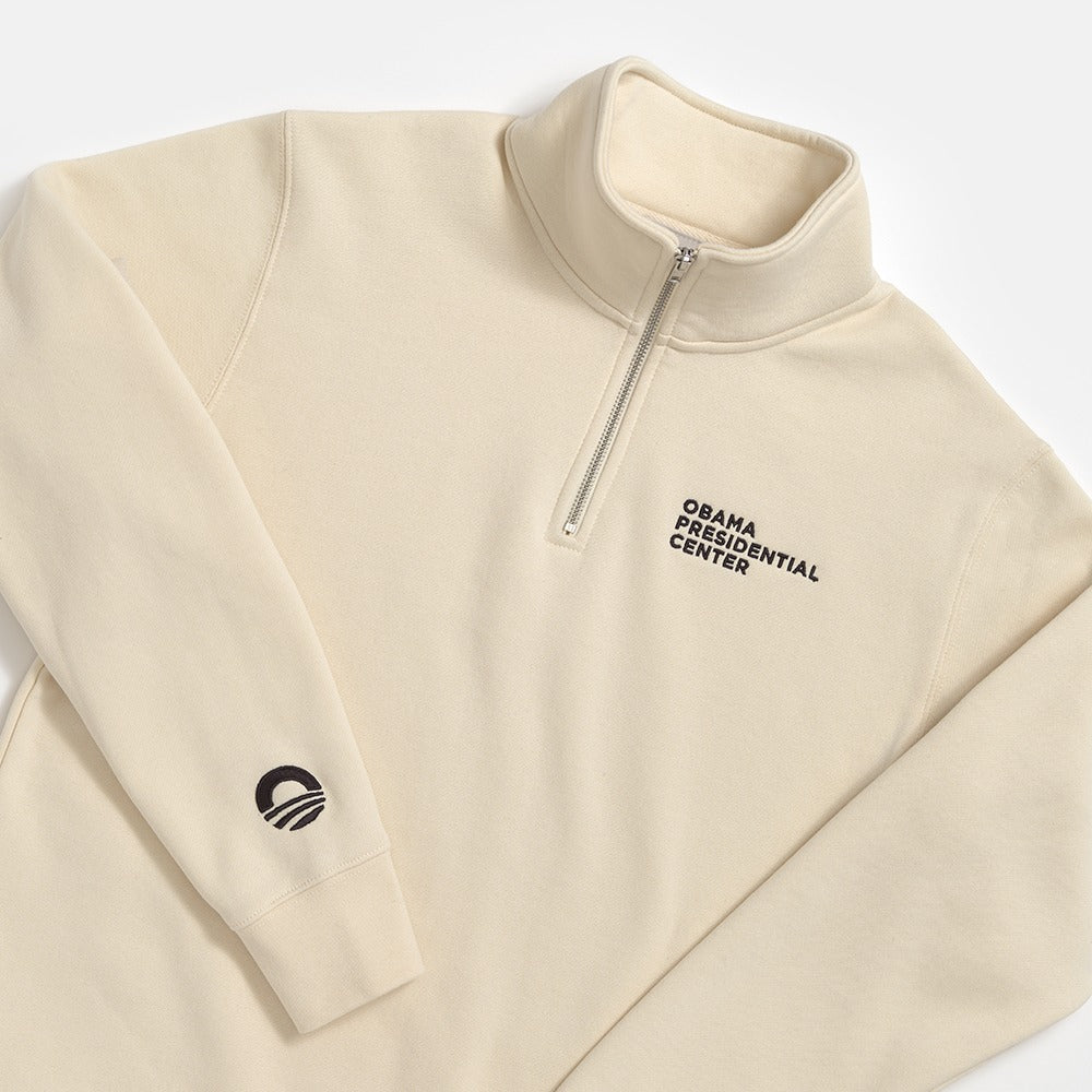 The Obama Presidential Center Quarter Zip Sweatshirt features a cream color, "Obama Presidential Center" embroidery on the left chest, and a small Obama logo near the left wrist.