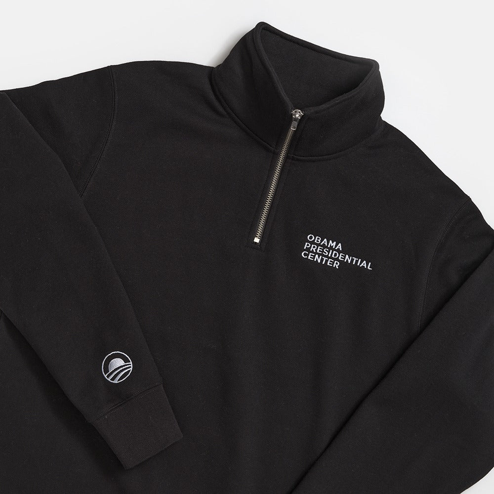 The Obama Presidential Center Quarter Zip Sweatshirt is a black pullover featuring "OBAMA PRESIDENTIAL CENTER" embroidered on the chest and a small Obama logo on the sleeve, shown against a white background.