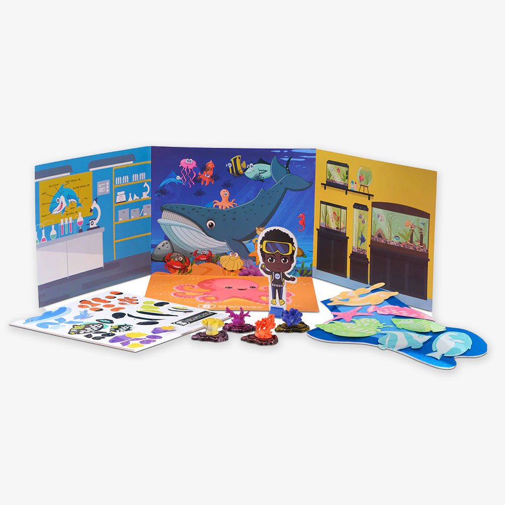 The Marine Biology STEAM Kit features a colorful aquarium-themed playset with illustrated backgrounds, sea creature stickers, a diver, paper fish, and small coral figures arranged on a white surface.