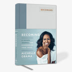 Becoming: A Guided Journal for Discovering Your Voice is an inspirational self-discovery journal by Michelle Obama, featuring a smiling cover photo of her seated on light blue and white, with a silver ribbon bookmark.
