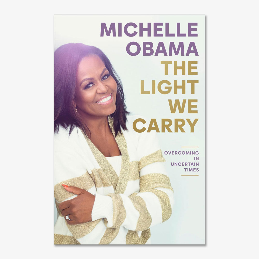 The cover of The Light We Carry: Overcoming In Uncertain Times by Michelle Obama shows her smiling in a white sweater with beige stripes.