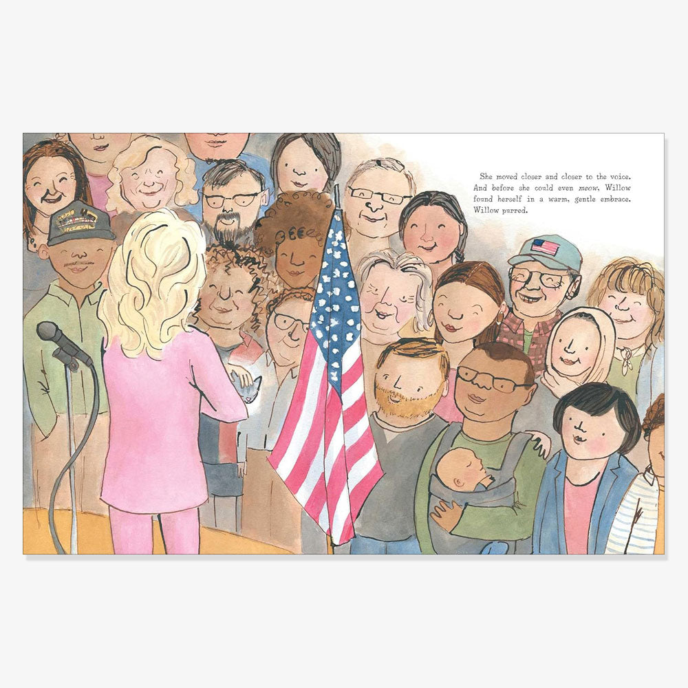 A woman in a pink suit with long blond hair stands at a podium next to an American flag, addressing a diverse, smiling crowd while promoting the children's book "Willow the White House Cat." Text is seen in the upper right corner.