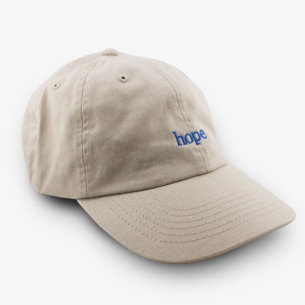 The Obama Presidential Center Hope Cap is beige with "hope" embroidered in small blue letters on the front. The cap is shown against a white background.