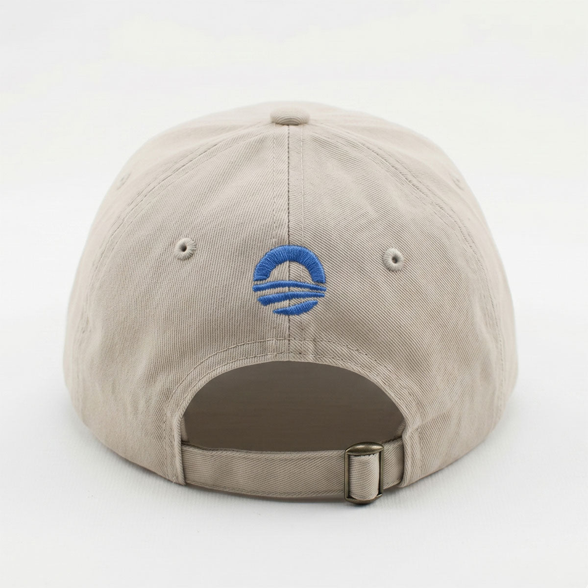 The Obama Presidential Center Hope Cap – Stone is a beige cap with a blue embroidered "O" logo and three horizontal lines, an adjustable strap with metal clasp, offering a stylish tribute to the Obama Foundation.