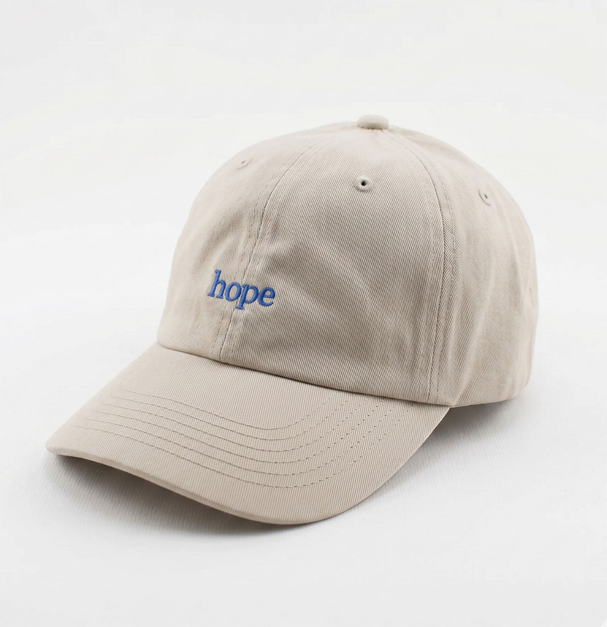 The Obama Presidential Center Hope Cap – Stone, featuring "hope" embroidered in blue lowercase letters on the front, rests on a plain white surface.