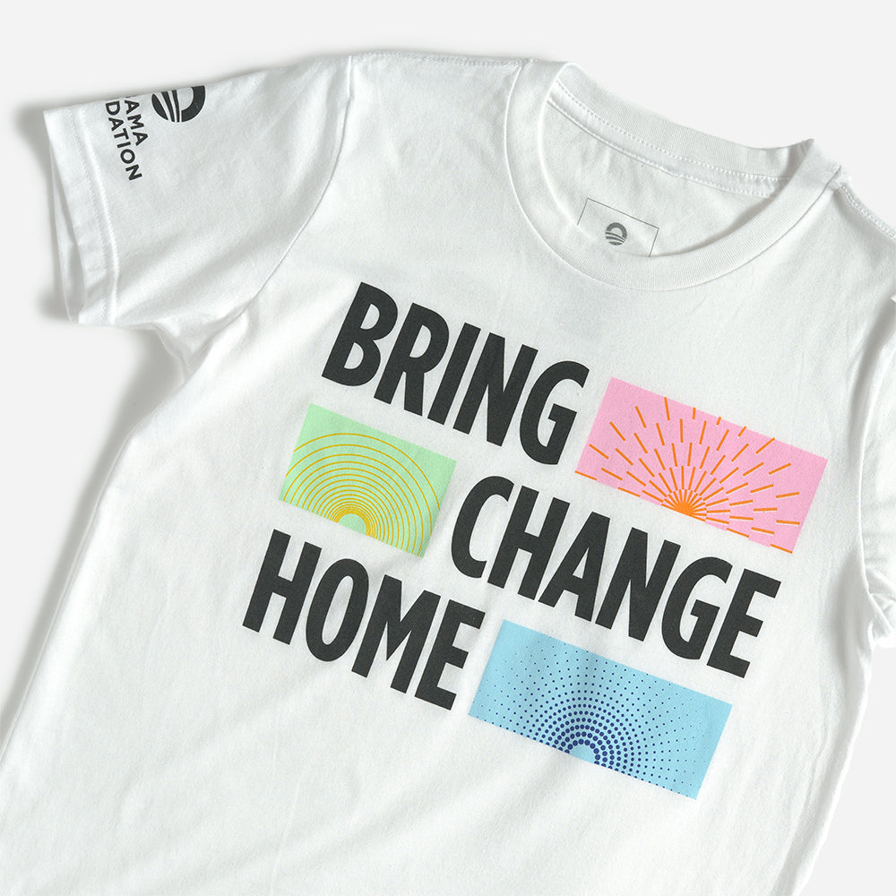 The Obama Foundation Youth T-Shirt features "BRING CHANGE HOME" in bold black text with green-yellow circles, orange rays, and blue dots beside each word. Inspired by the Obama Foundation, with the AMA FOUNDATION logo on the sleeve.
