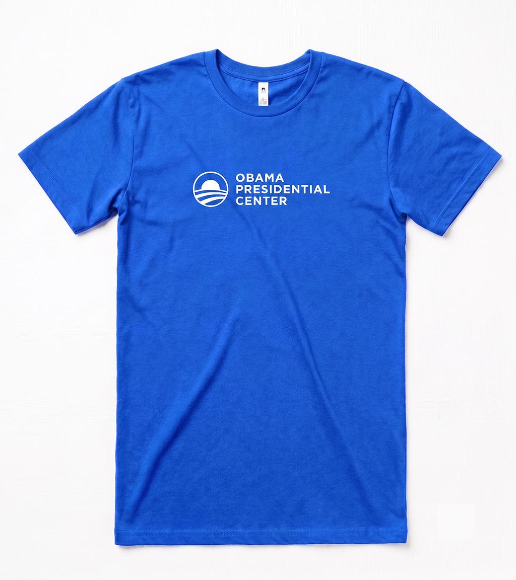 The Obama Presidential Center Logo T-shirt - Royal features the white logo and text on the chest, celebrating the Foundation’s South Side work. Displayed flat on a white surface, this royal blue tee shows your support.