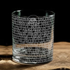 The Obama Presidential Center "You Are America" Speech Rocks Glass rests on a wooden surface, featuring tightly etched uppercase text from the speech wrapped around its clear glass. The words form a striking design against a black background.