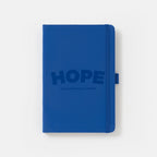 The Obama Presidential Center Hope Journal is a navy blue notebook with the HOPE wordmark and center logo on the cover, plus an elastic band closure and a pen loop on the right side.