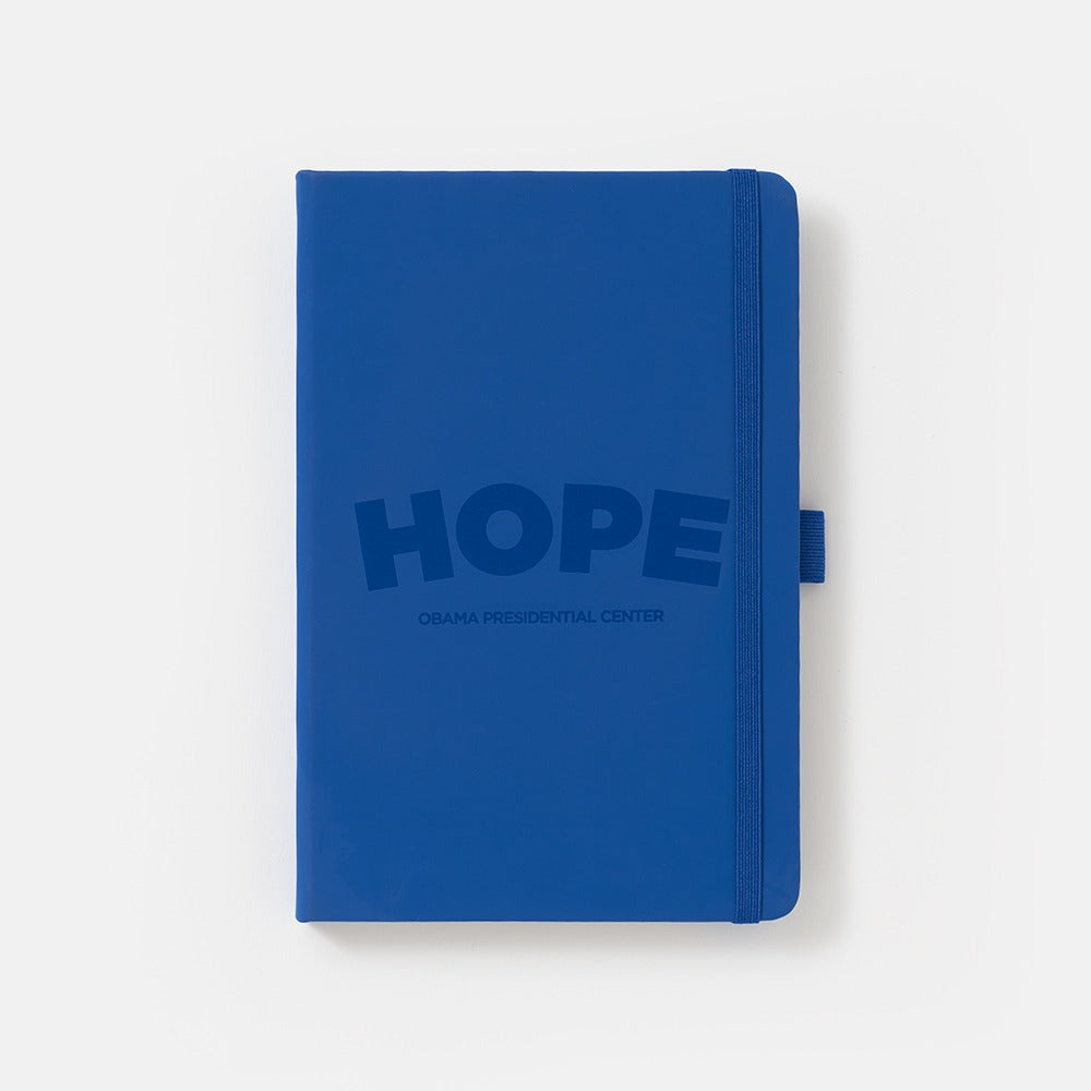 The Obama Presidential Center Hope Journal is a navy blue notebook with the HOPE wordmark and center logo on the cover, plus an elastic band closure and a pen loop on the right side.