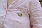 A person wears a light pink button-up shirt with the Skyline Heart Pin—a colorful enamel heart shaped like Chicago’s skyline and featuring the words SHOW UP—attached to the chest pocket.