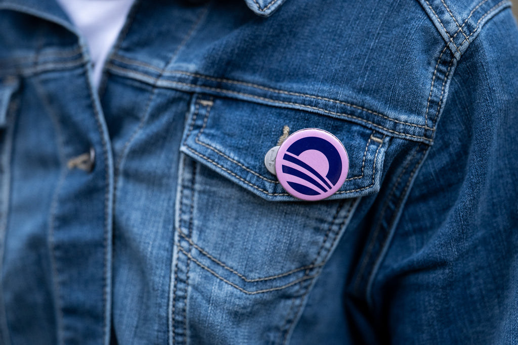Close-up of a person wearing a denim jacket with an Obama Foundation Pin Set button, showing their support, pinned to the pocket.