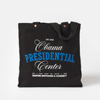The Obama Presidential Center Script Tote is a black canvas bag with “Obama Presidential Center Est. 2026” in white and blue, plus Inspire Empower & Connect and a Chicago address below—a stylish Obama Foundation accessory for any outing.