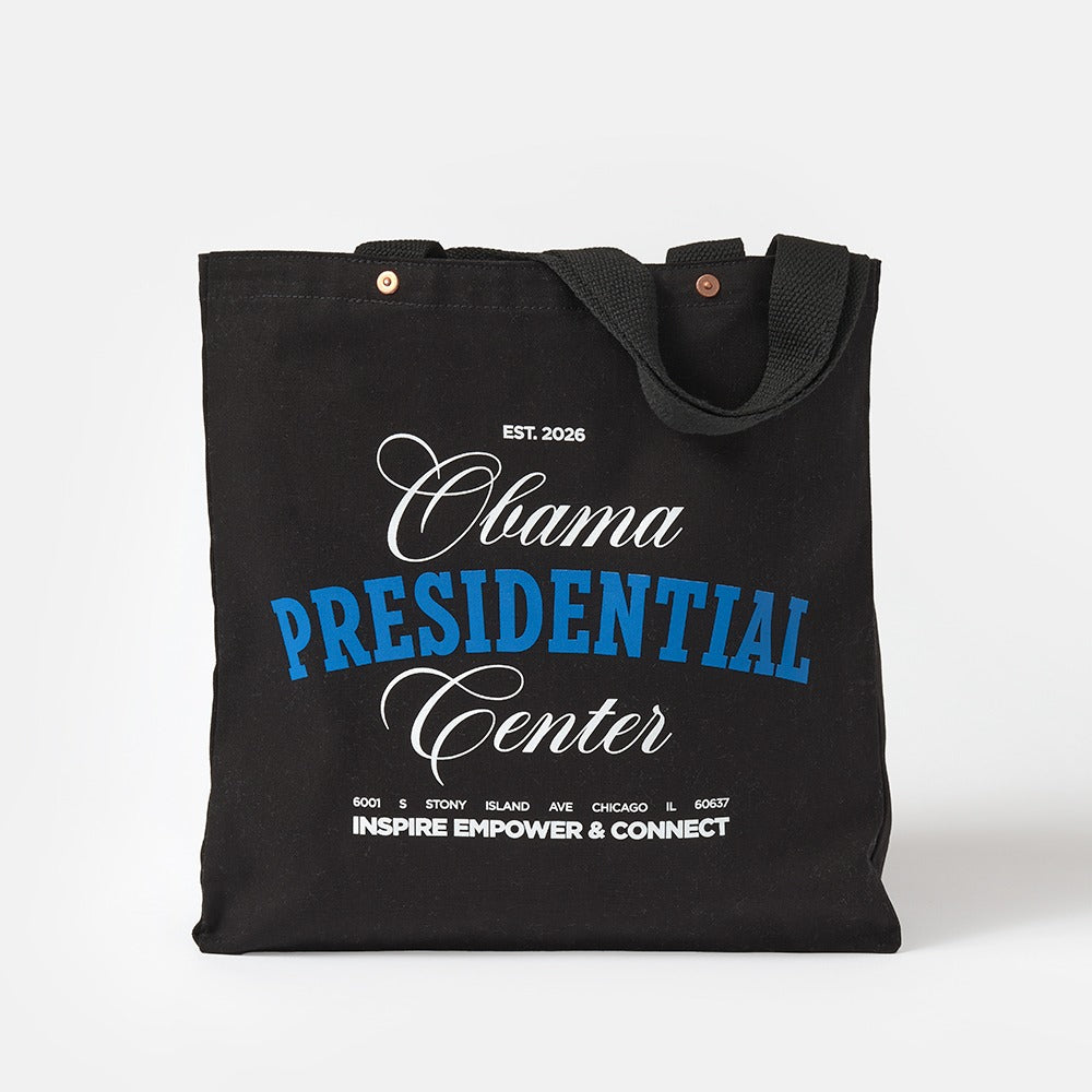 The Obama Presidential Center Script Tote is a black canvas bag with “Obama Presidential Center Est. 2026” in white and blue, plus Inspire Empower & Connect and a Chicago address below—a stylish Obama Foundation accessory for any outing.