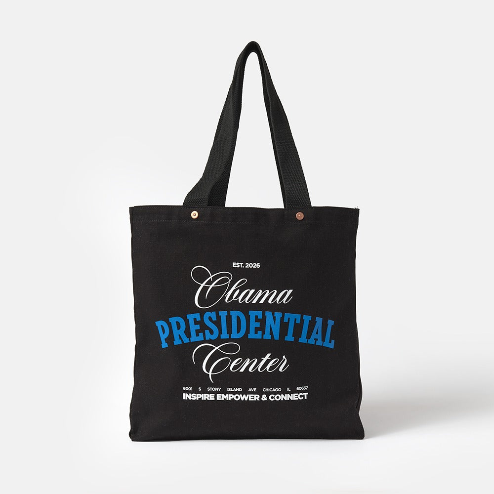 The Obama Presidential Center Script Tote is a black canvas bag with "Obama Presidential Center" in white and blue text, plus "Inspire Empower & Connect" and Obama Foundation locations printed in small white font at the bottom.