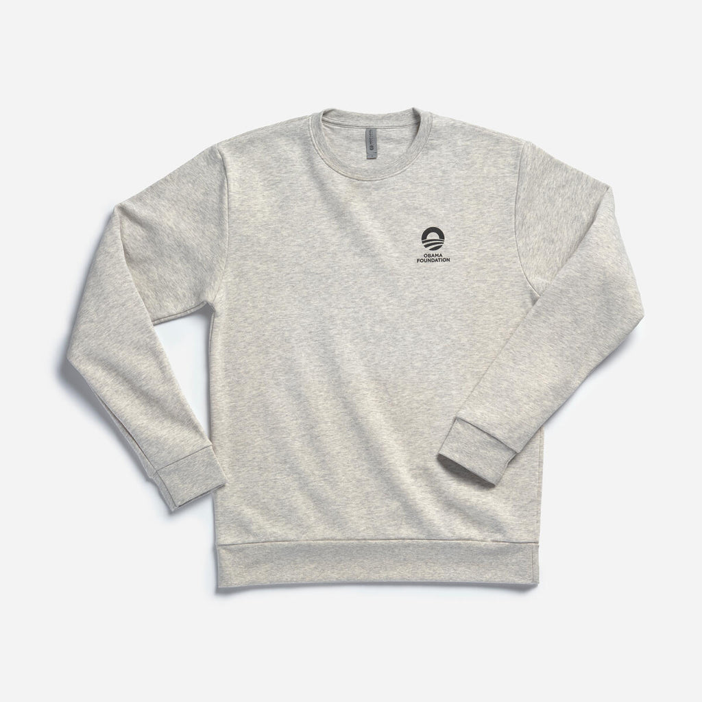 The Obama Foundation Sweatshirt is a light gray, long-sleeve crewneck with a small black logo and text on the left chest, shown laid flat on a white background.