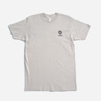 The Obama Foundation T-Shirt is a plain light gray crewneck laying flat on a white surface, featuring a small black graphic and the Obama Foundation’s rising sun logo with text on the left chest.