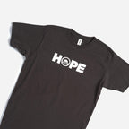 The Obama Foundation "Hope" T-shirt is black with bold white HOPE lettering; the O has a rising sun logo with red and blue stripes, inspired by the classic Obama Foundation design.