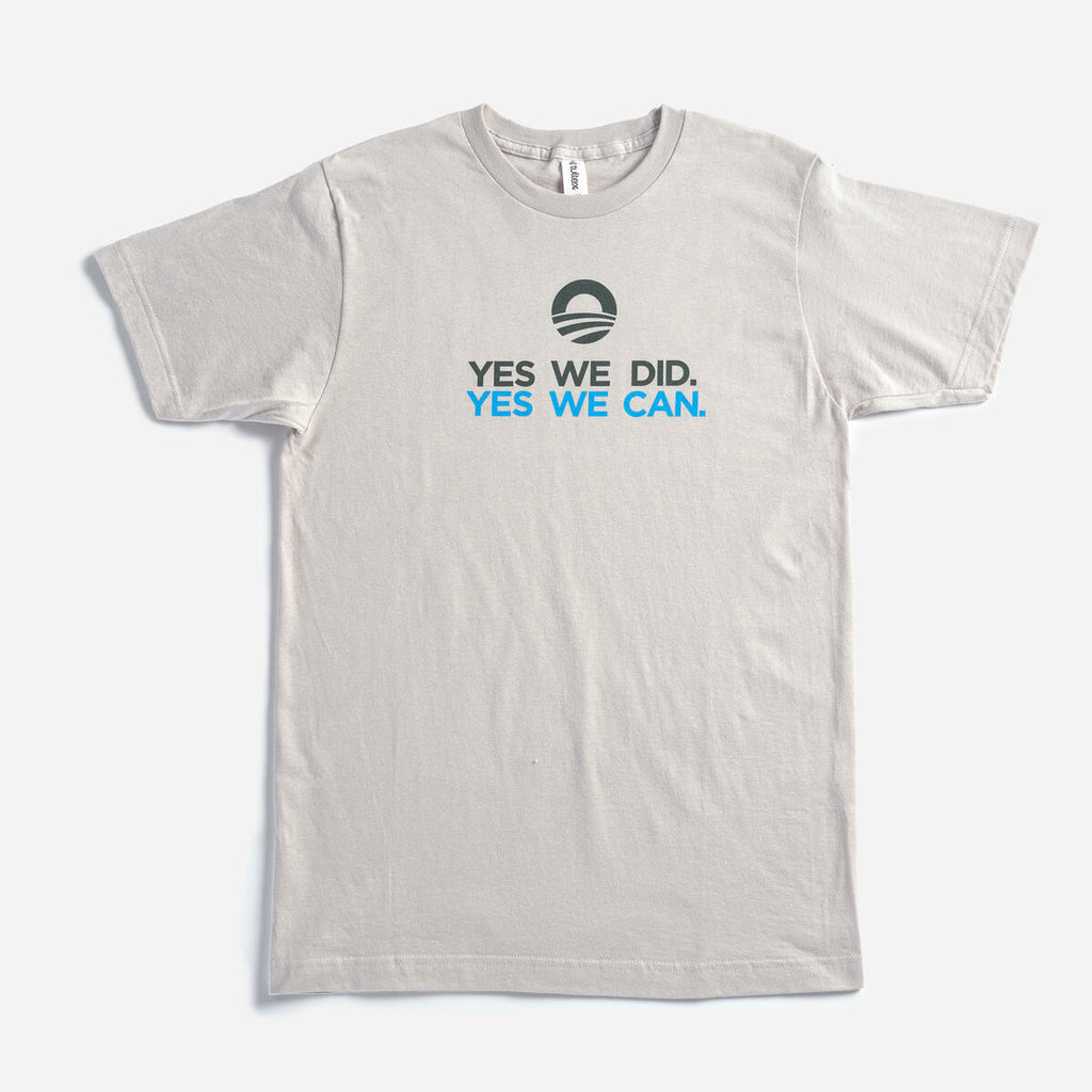 The "Yes We Can" T-shirt is a light gray tee featuring the Obama campaign logo above "YES WE DID. YES WE CAN." in bold black and blue, inspired by President Obama's farewell address and supporting the Obama Foundation.