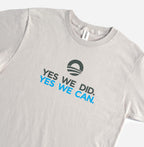 The "Yes We Can" T-shirt is a light gray shirt featuring the Obama Foundation campaign logo above “YES WE DID.” in black and “YES WE CAN.” in blue, celebrating Barack Obama's iconic farewell address.