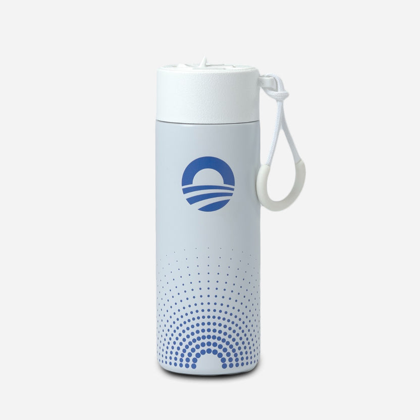 The Obama Foundation Water Bottle, a white stainless steel bottle with a blue circular logo and dot pattern, features a carrying strap on its leak-resistant straw lid and stands upright against a plain light gray background.